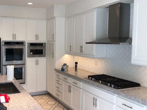 A finished white kitchen with a double wall oven, a built-in microwave, a vented hood and a gas cooktop.